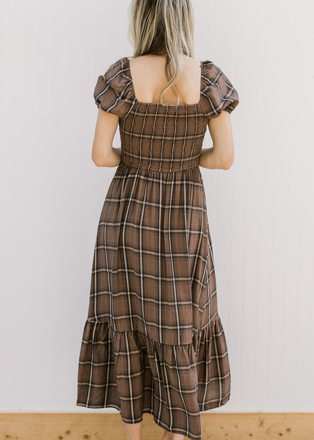 Back view of Model wearing a brown and cream plaid midi with a smocked bodice and short sleeves. 