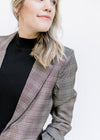 Close up of classic detailing on a Model wearing a brown plaid blazer with 3/4 tacked sleeves. 