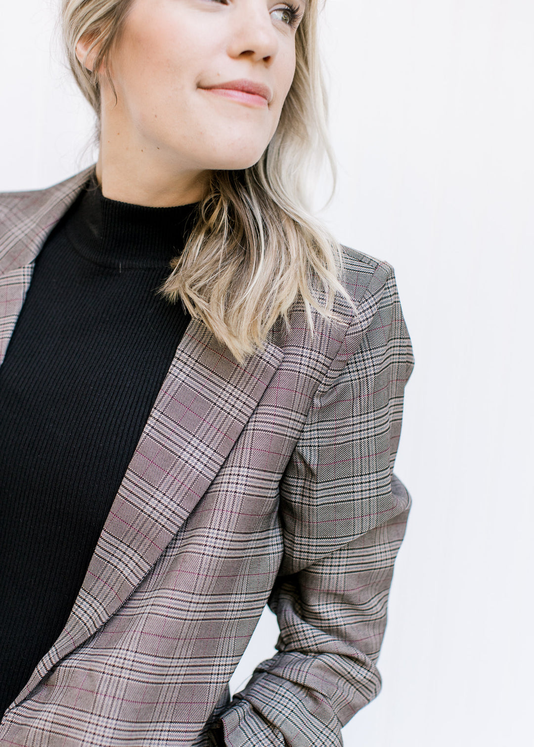 Close up of classic detailing on a Model wearing a brown plaid blazer with 3/4 tacked sleeves. 