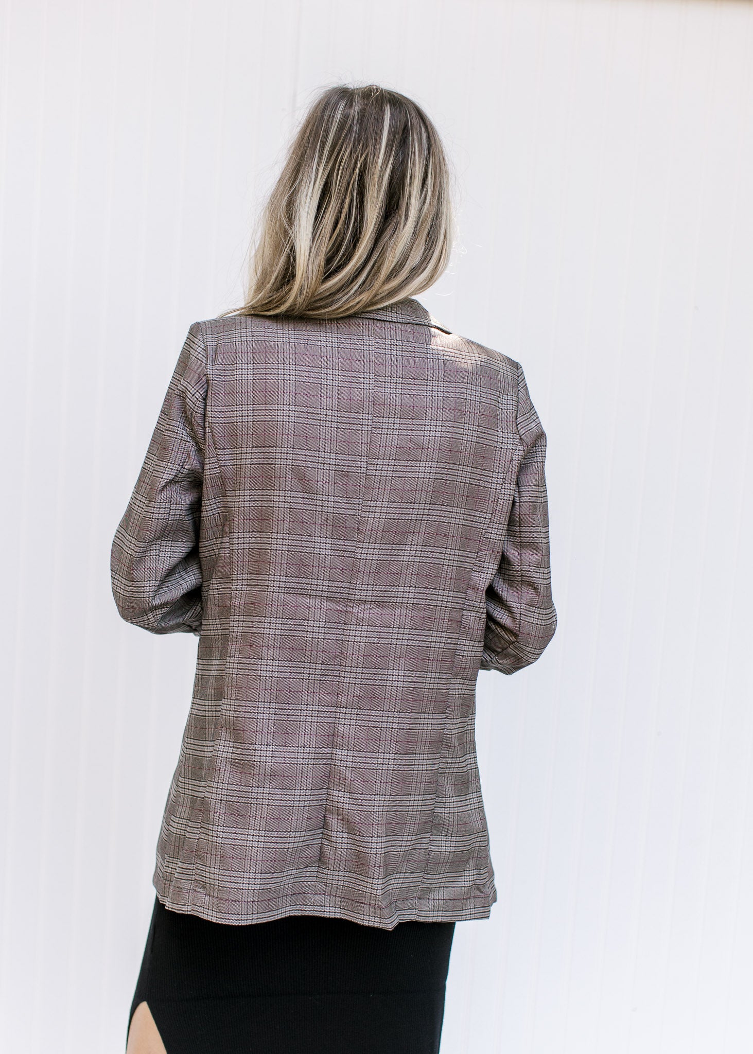 Back view of Model wearing a brown plaid blazer with 3/4 tacked sleeves and classic detailing. 
