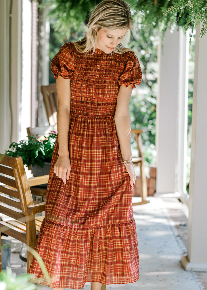 Model wearing a rust, tan and maroon plaid midi with a smocked bodice and bubble short sleeves. 