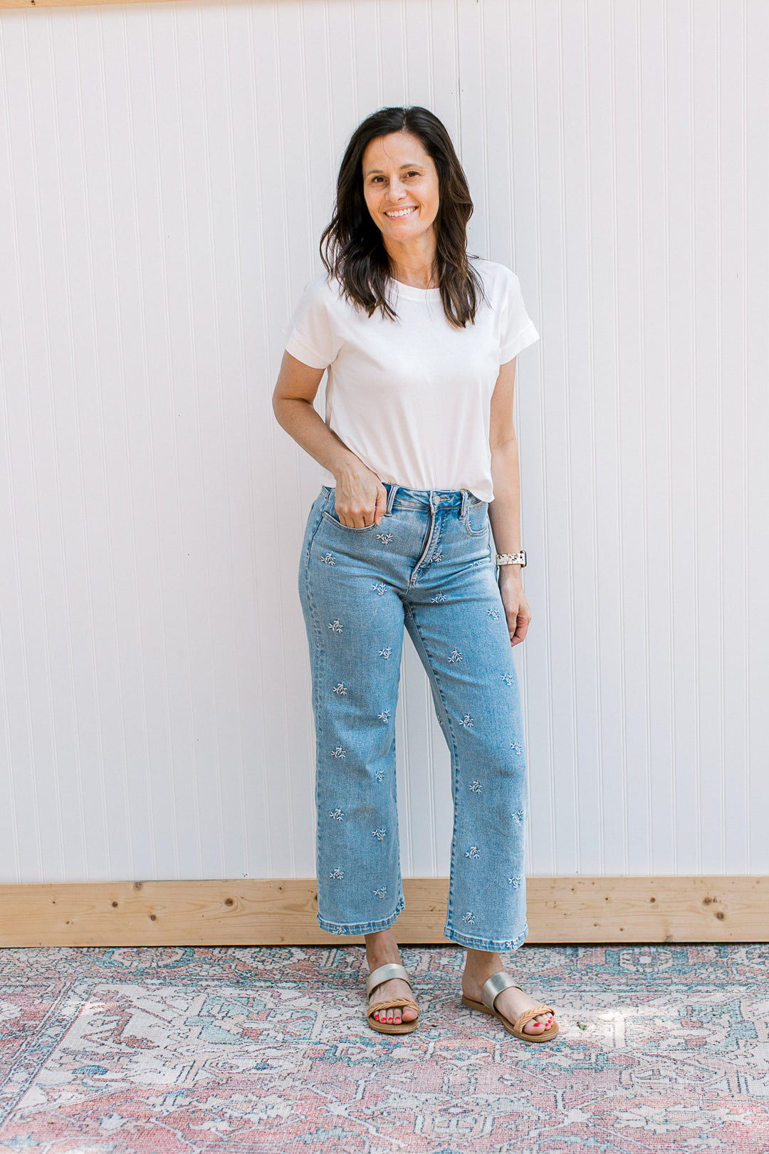 Model wearing jeans, sandals and a white tee with short sleeves and a slightly cropped fit.