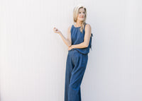 Model wearing a denim blue set with a spaghetti strap top and wide legs bottoms with pleating. 