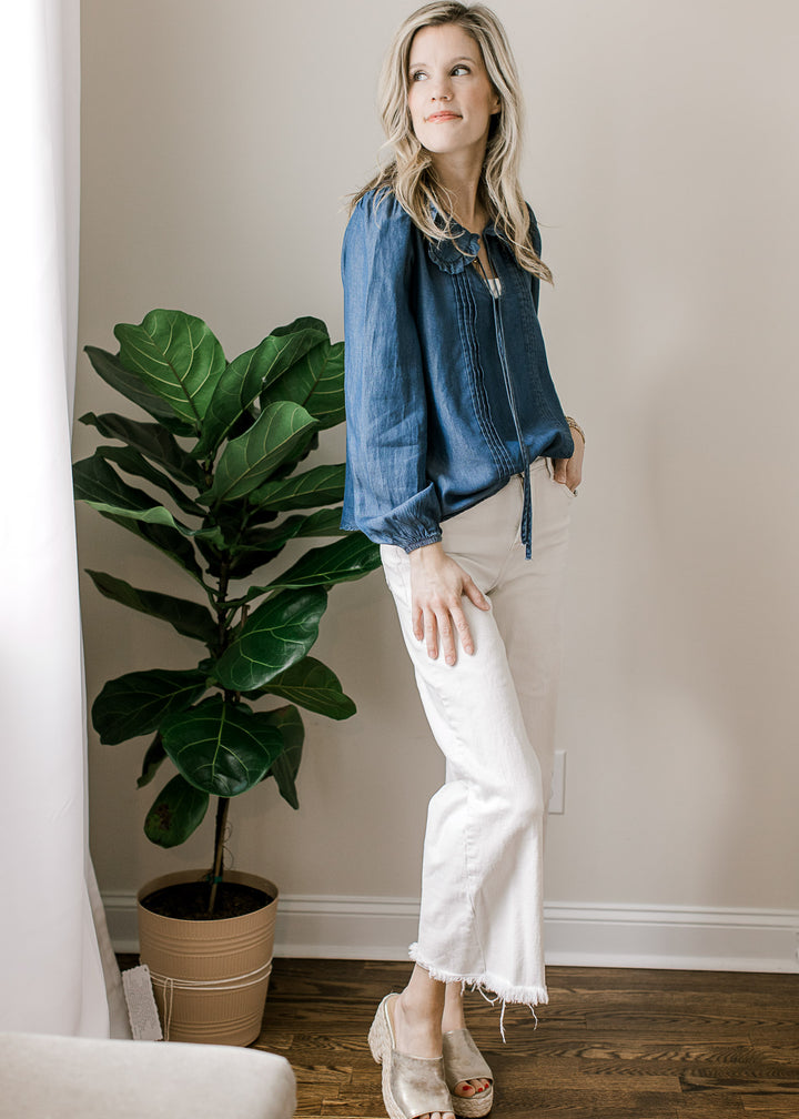 Model wearing white pants and a blue top with flap collar, long sleeves and v-neck with tie. 