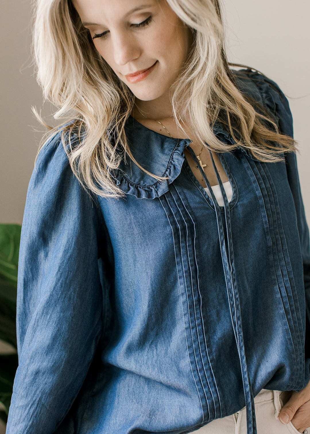 Close up of flap collar with a ruffle and tie v-neck on a long sleeve blue top with pleated bodice. 
