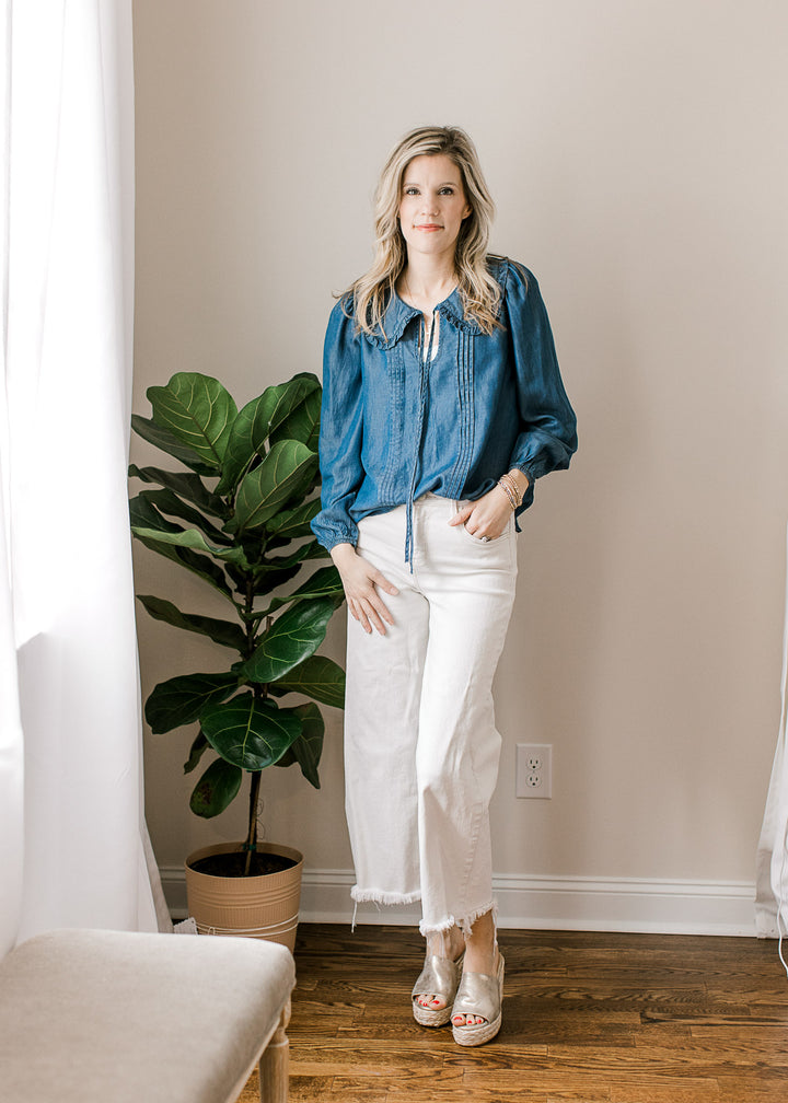 Model wearing white pants, wedges and a long sleeve blue top with pleated bodice and v-neck.