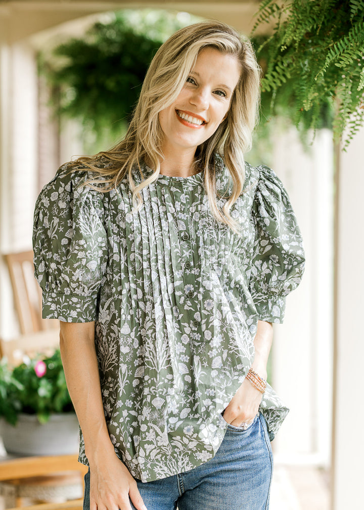 Model in an olive top with a blue print, micro pleat details, button front and short puff sleeves. 