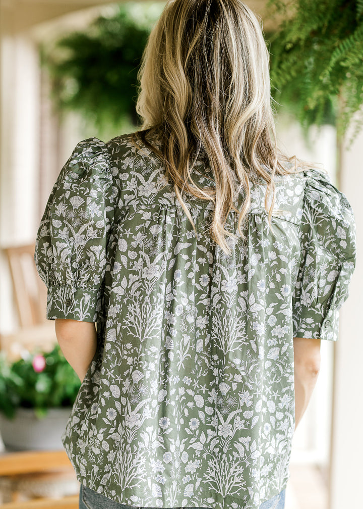 Back view of Model wearing an olive green top with a blue print and short puff sleeves. 
