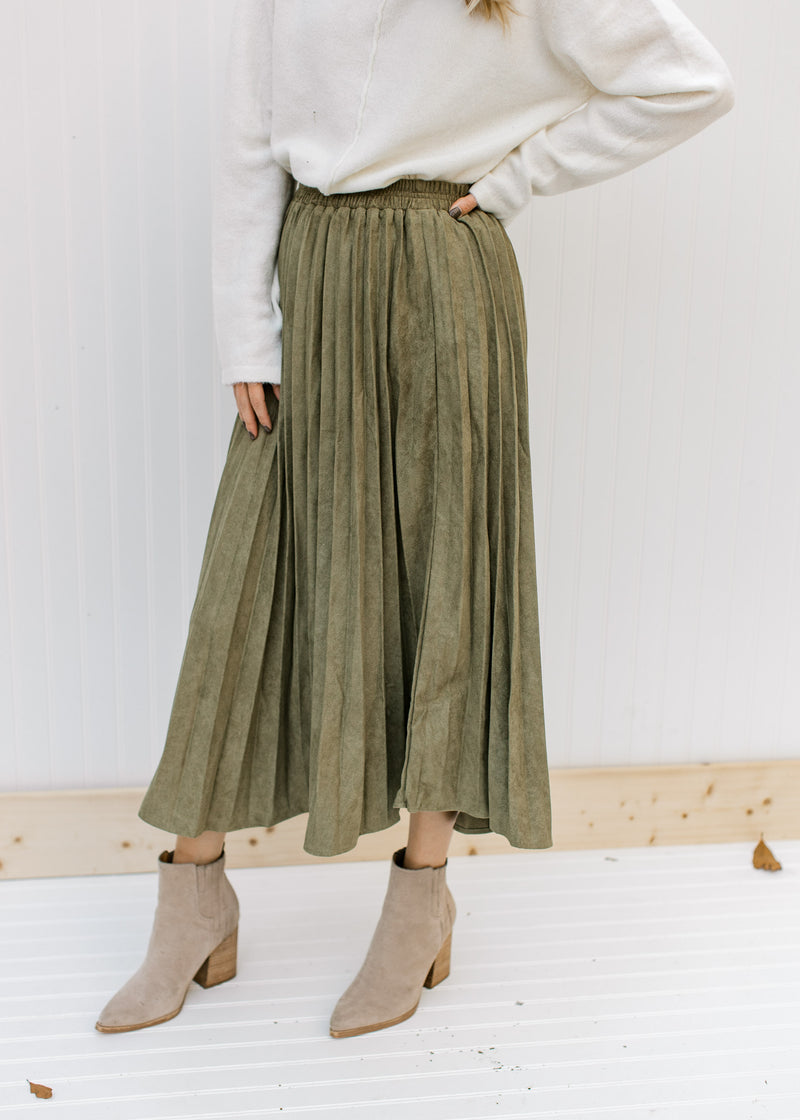 Model wearing a pleated olive skirt with a velvet material, elastic waistband and a midi length. 