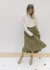 Model wearing cream top with a pleated olive skirt with a velvet material and an elastic waistband. 