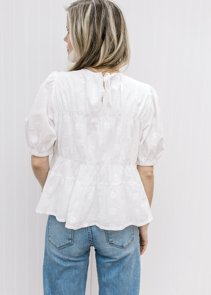 Back view of Model wearing a white top with textured details, round neck, and tie keyhole closure.