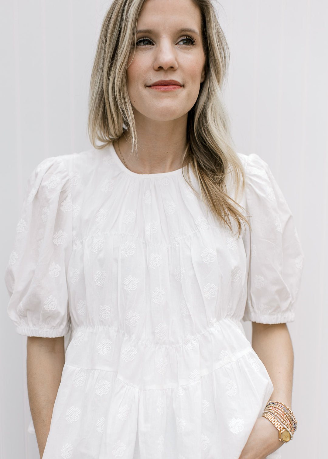 Model wearing a white top with textured details, round neck, short sleeves and pleating detail.