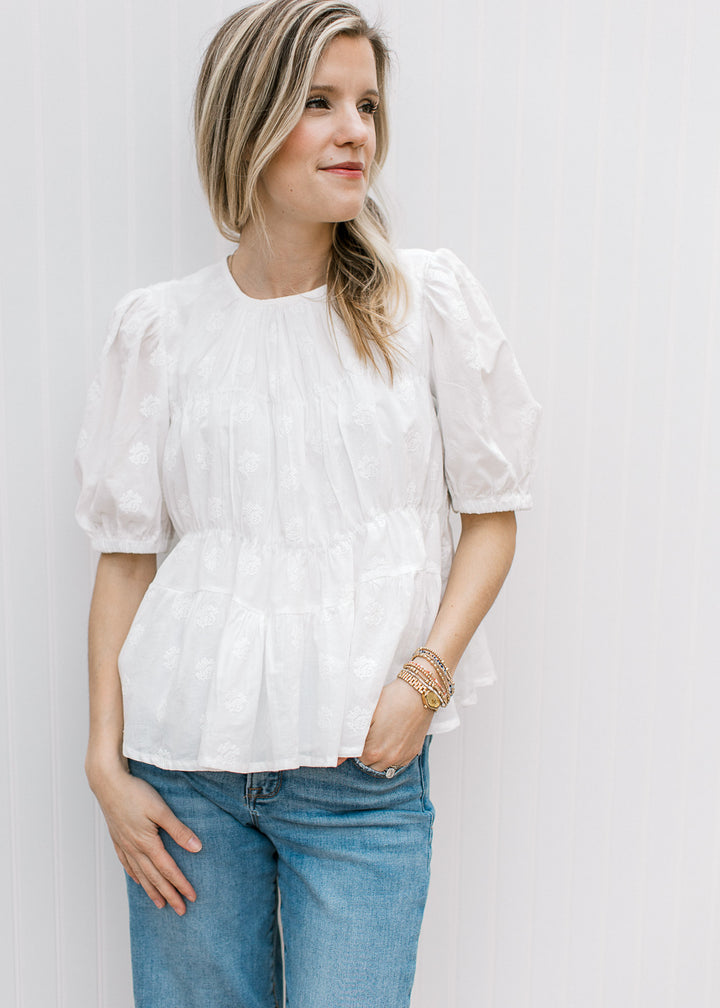 Model wearing jeans and a white top with texturing, round neck, bubble short sleeves and pleating.