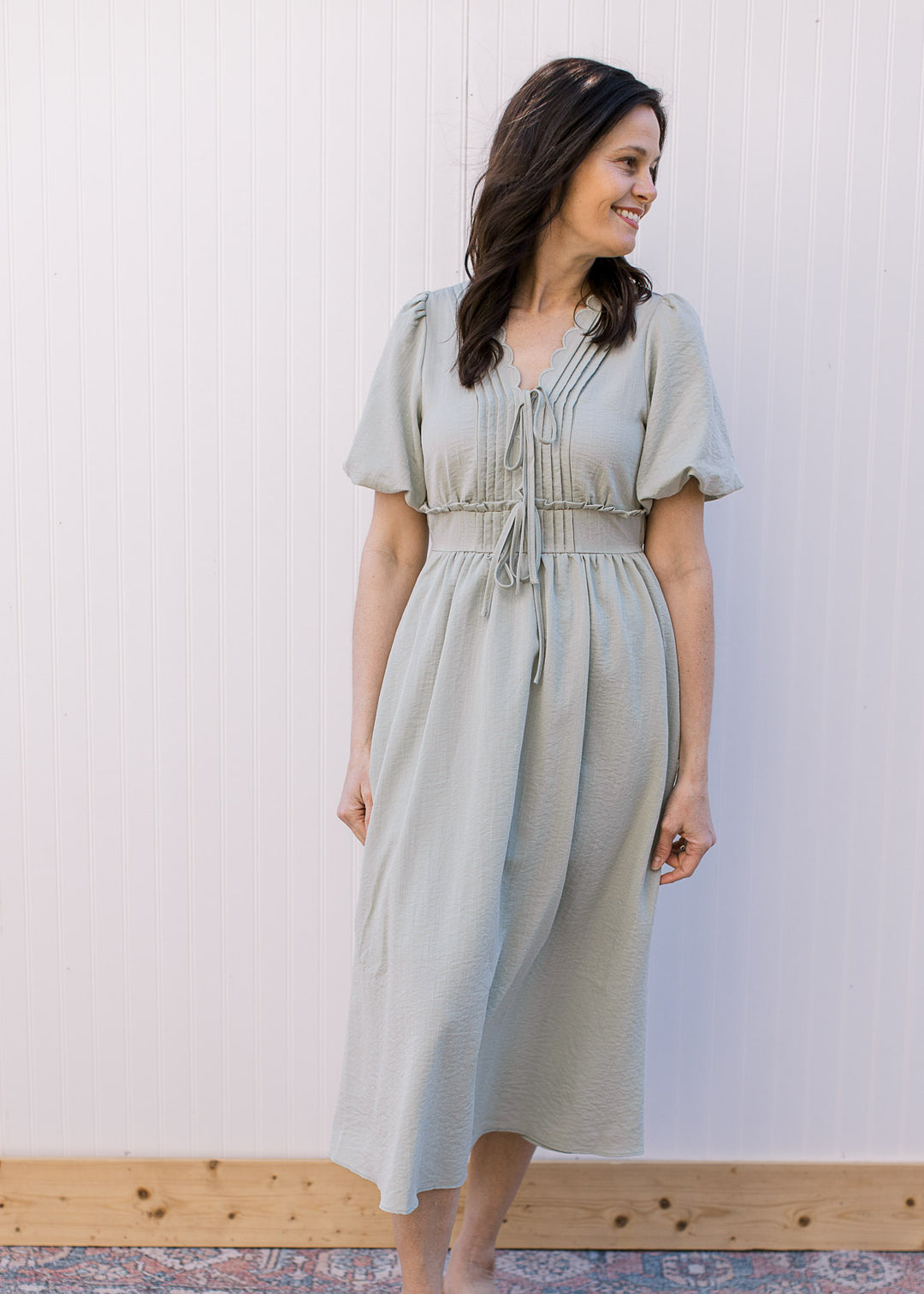 Model wearing a sage midi with scalloping and pleating detail, waist with ruffle and short sleeves.