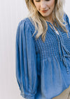 Model wearing a denim colored top with micro-pleated design, v-neck with a tie and 3/4 sleeves.