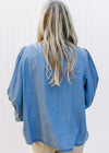 Back view of model wearing a denim colored top with pleated shoulders and 3/4 sleeves. 