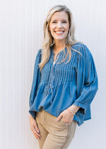 Model wearing a flowy denim top with micro-pleated design, v-neck with a tie and 3/4 sleeves.