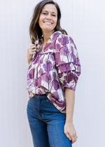 Model wearing a cream v-neck top with plum floral, ric-rac detail a collar and 3/4 sleeves. 