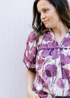 Close up of v-neck and ric-rac detail on a cream top with plum colored flowers and 3/4 sleeves. 