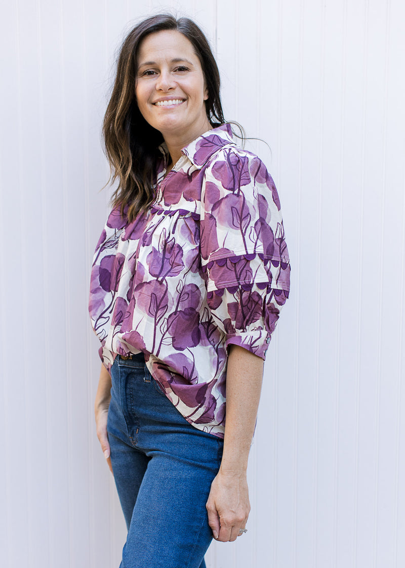 Model wearing jeans with a cream top with plum floral, ric-rac detail a collar and 3/4 sleeves. 