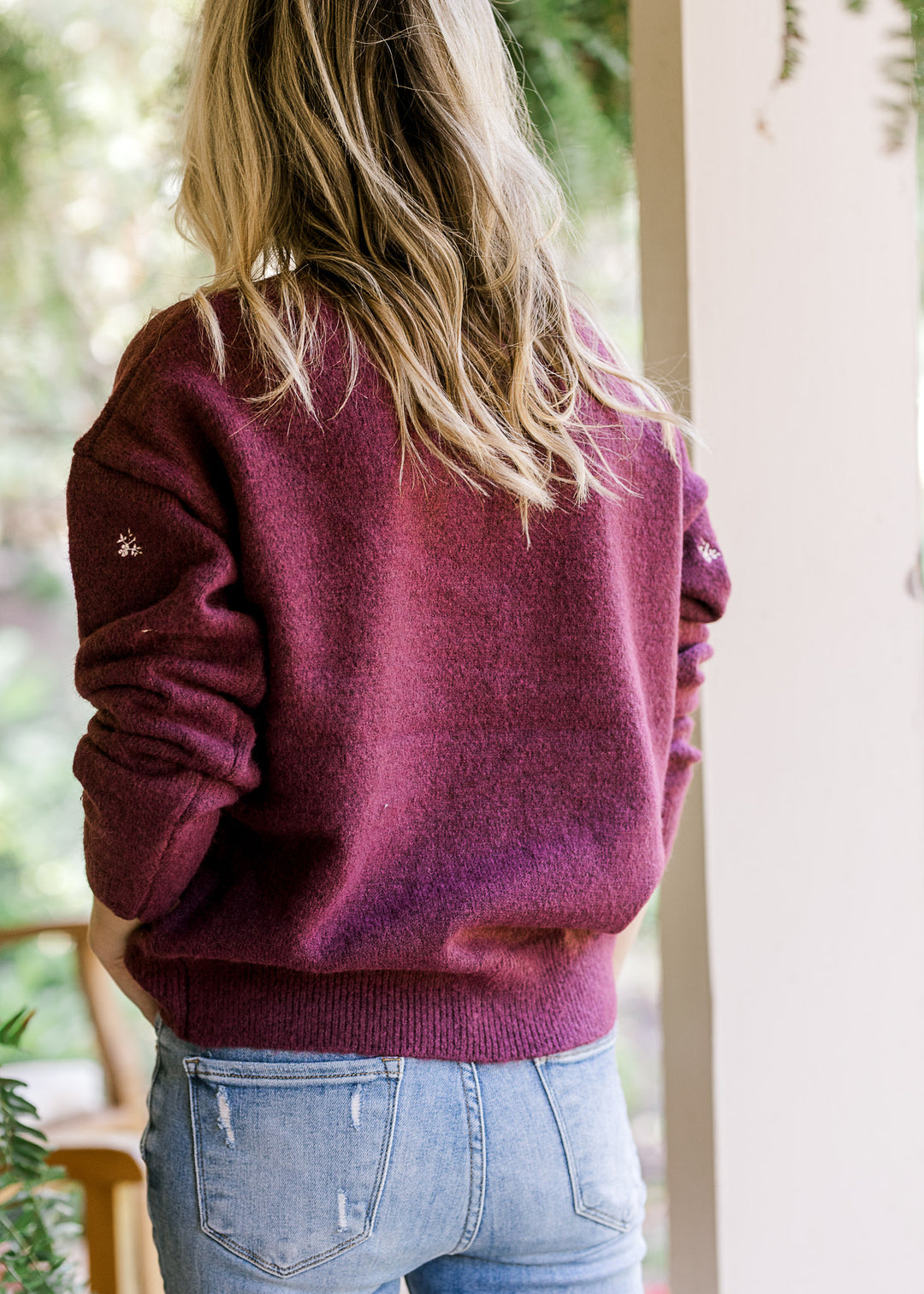 Back view of Model wearing a long sleeve plum sweater with cream flowers a round neck. 