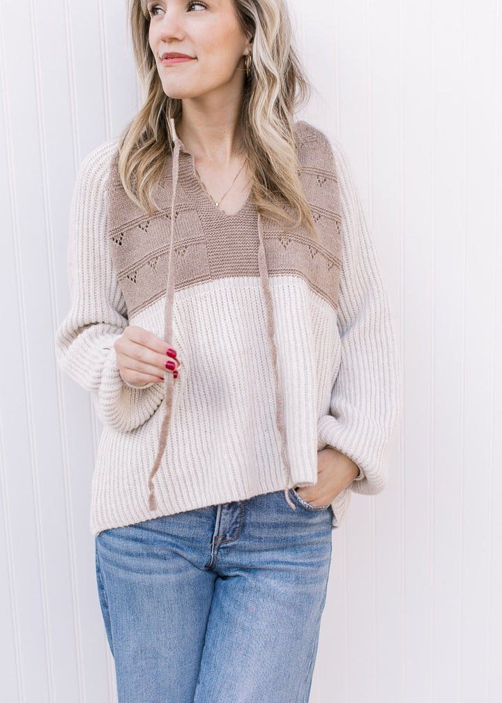 Model wearing a cream and taupe sweater with long sleeves with cuff and drawstring at v-neck.
