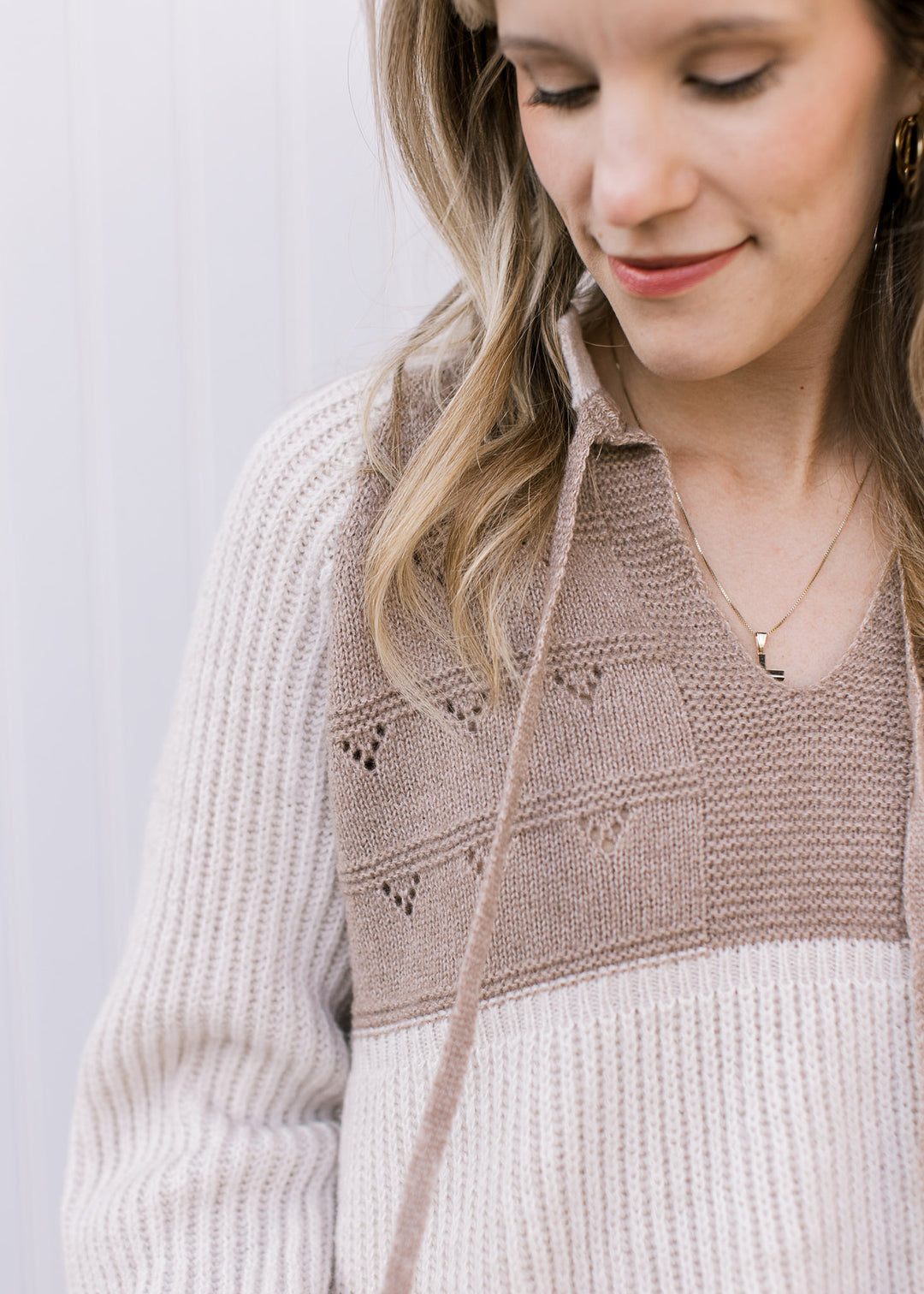 Close up of open knit and v-neck with drawstrings on a cream and taupe long sleeve sweater. 