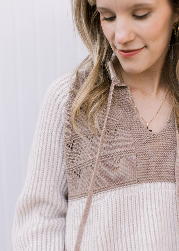 Close up of open knit and v-neck with drawstrings on a cream and taupe long sleeve sweater. 