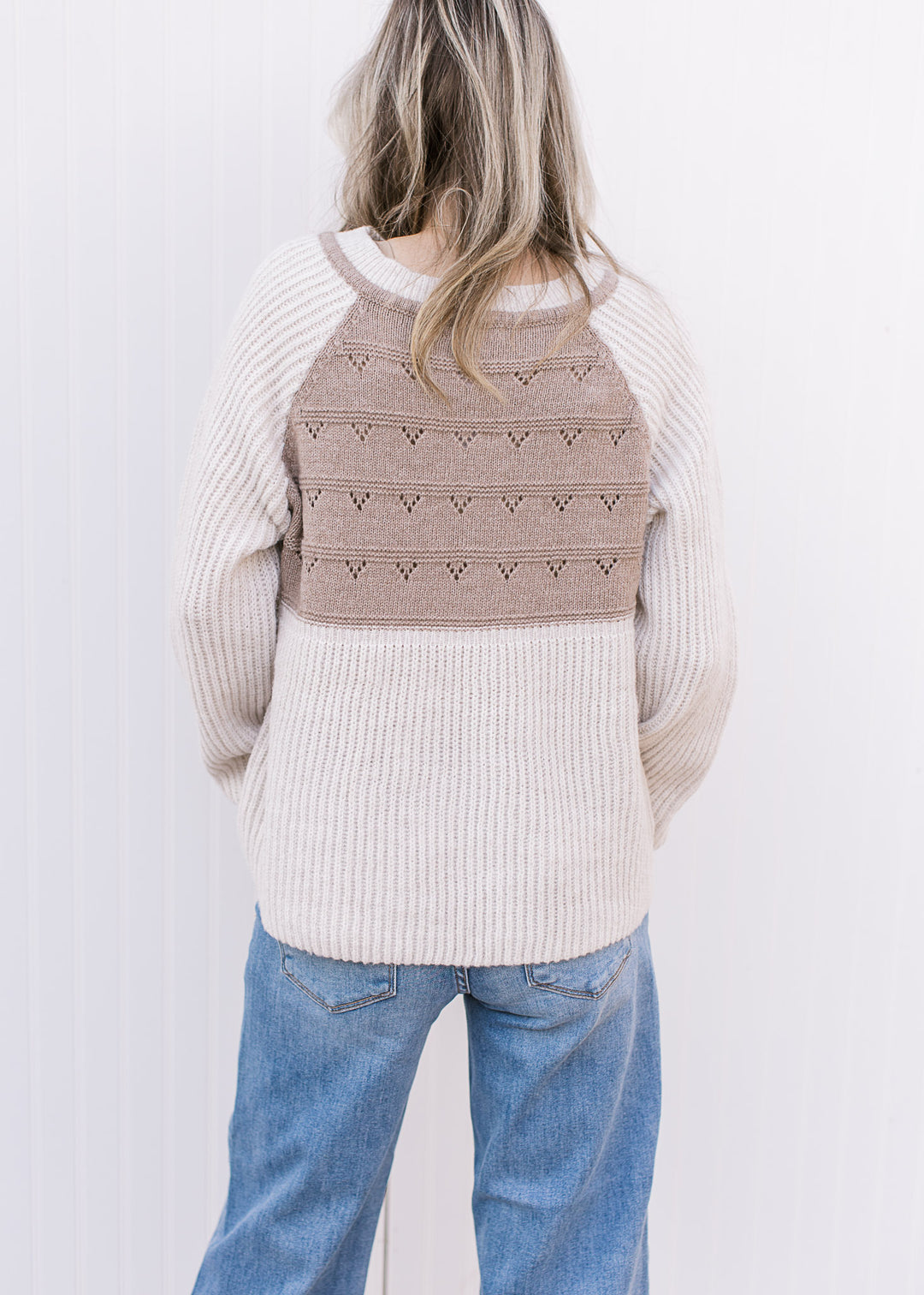 Back view of Model wearing a cream and taupe sweater with long sleeves and drawstring at v-neck.
