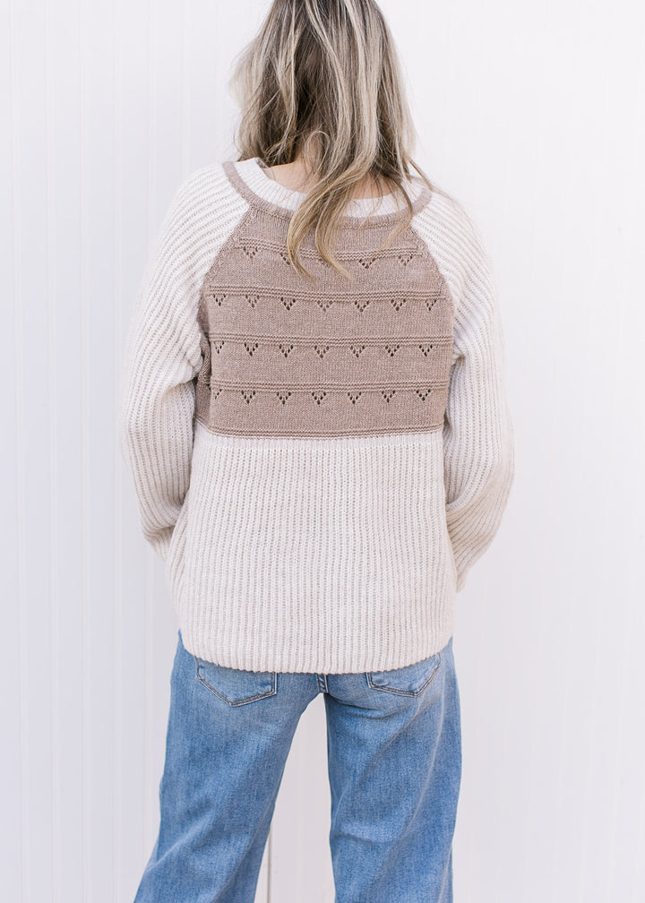 Back view of Model wearing a cream and taupe sweater with long sleeves and drawstring at v-neck.
