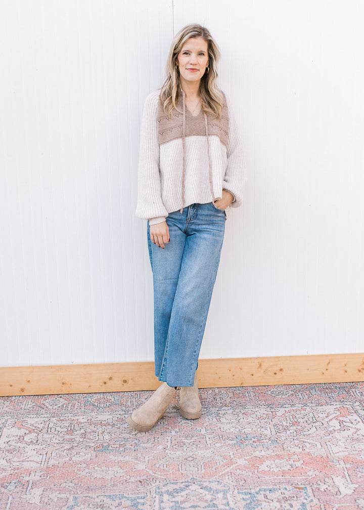 Model wearing jeans, booties and a long sleeve cream and taupe sweater with drawstring at the neck.
