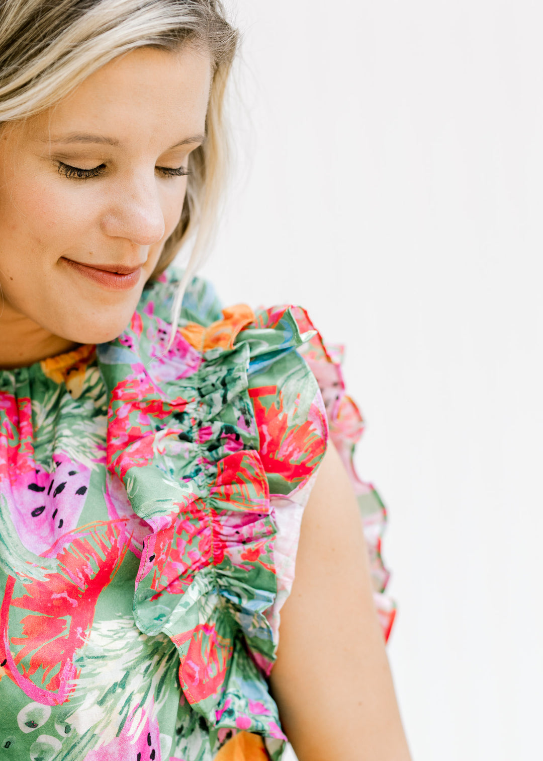 Close up view of ruffle cap sleeves on a model wearing a green top with bright food design. 