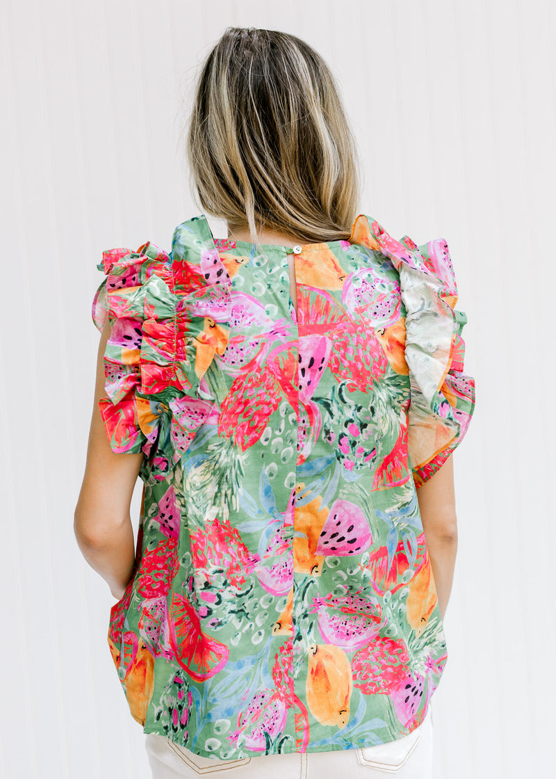 Back view of Model wearing a green top with a bright pattern, ruffle sleeves and a keyhole closure. 