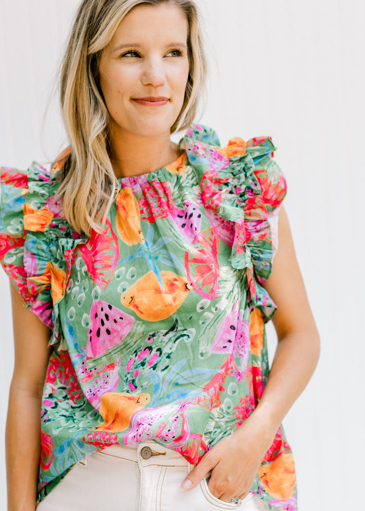 Model wearing a green top with bright food pattern and ruffle cap sleeves.