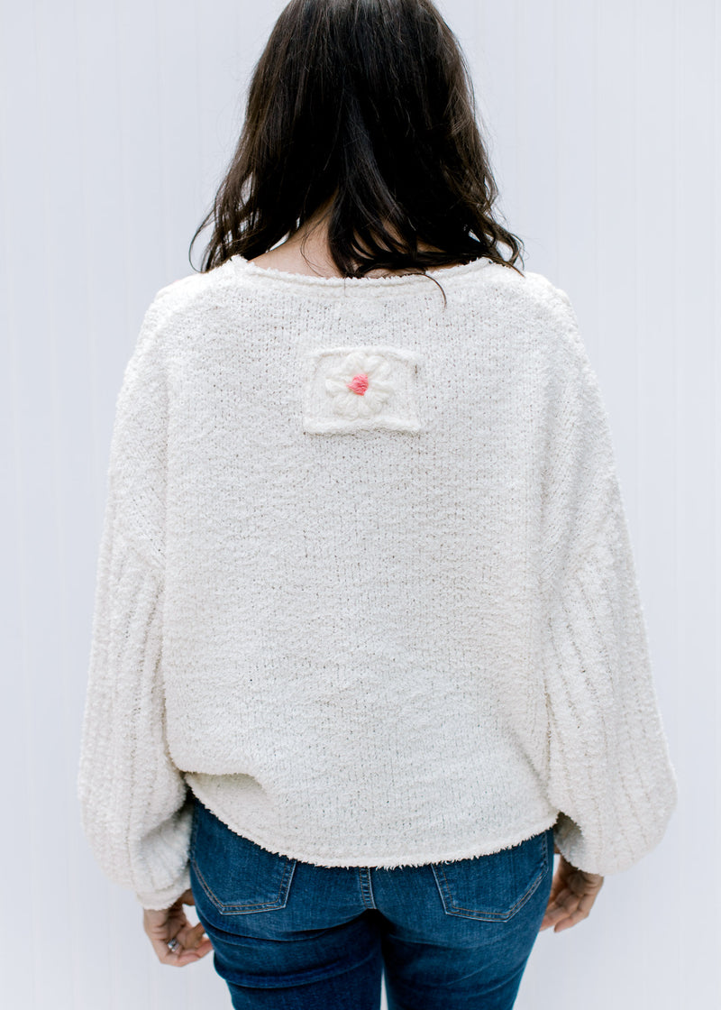 Back view of Model wearing an ivory sweater with textured flowers and  ribbed bubble long sleeves. 