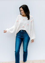 Model wearing jeans with an ivory sweater with textured flowers with pink center and rolled hem.  
