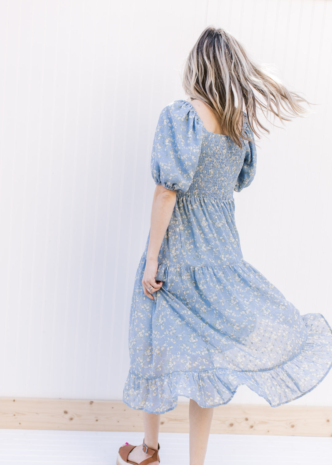 Model wearing a baby blue tiered dress with white poppy flowers, square neck and bubble sleeves.