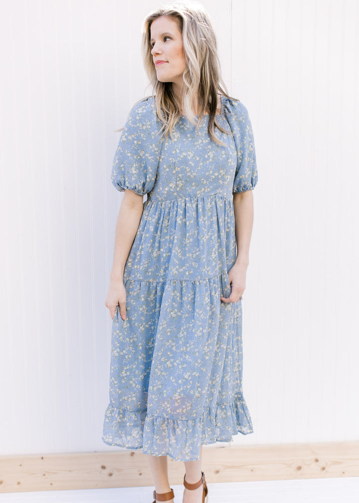 Model wearing a baby blue tiered dress with white flowers, square neckline and bubble short sleeves.
