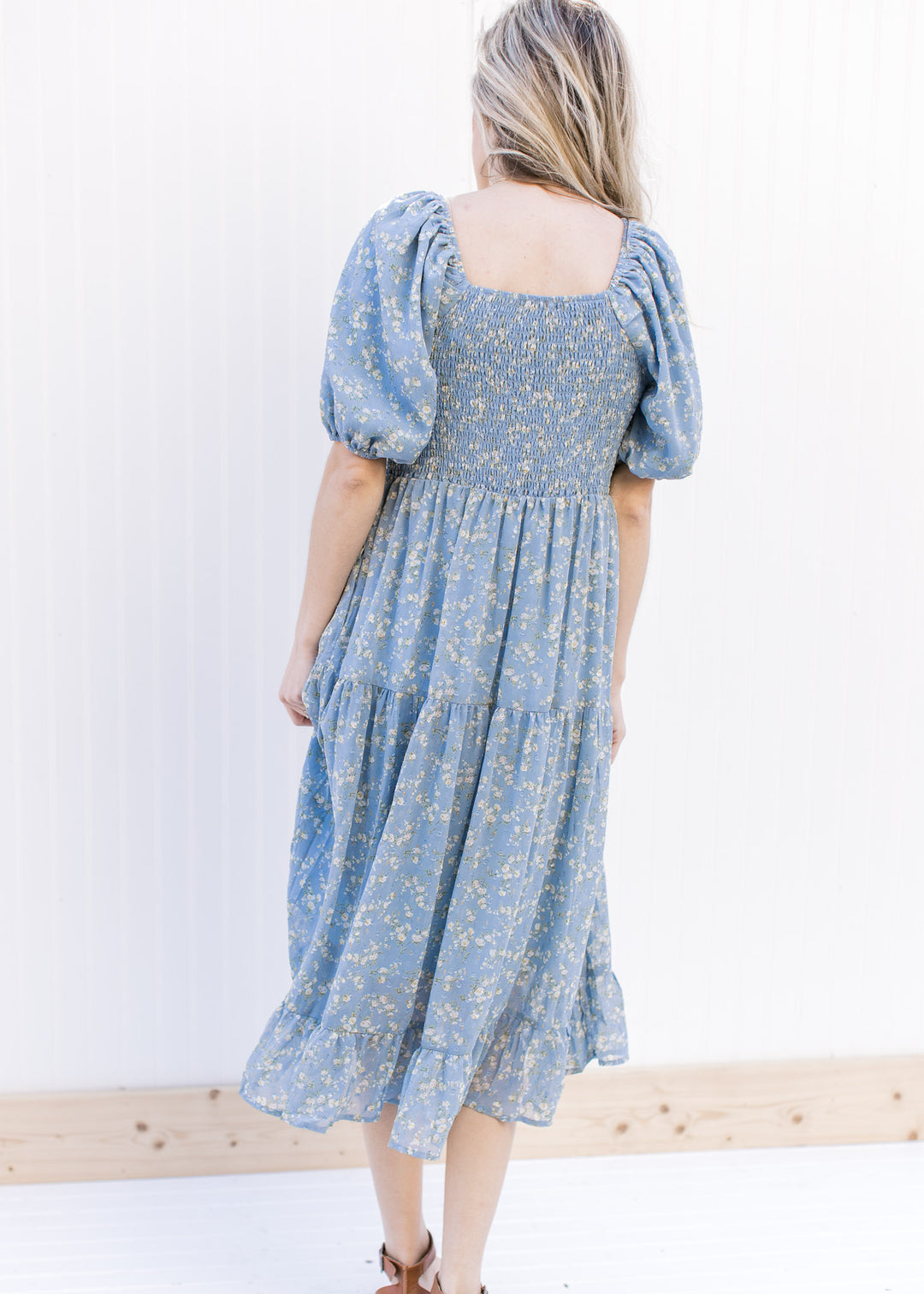 Back view of baby blue midi with white flowers, a smocked bodice, square neck and short sleeves.