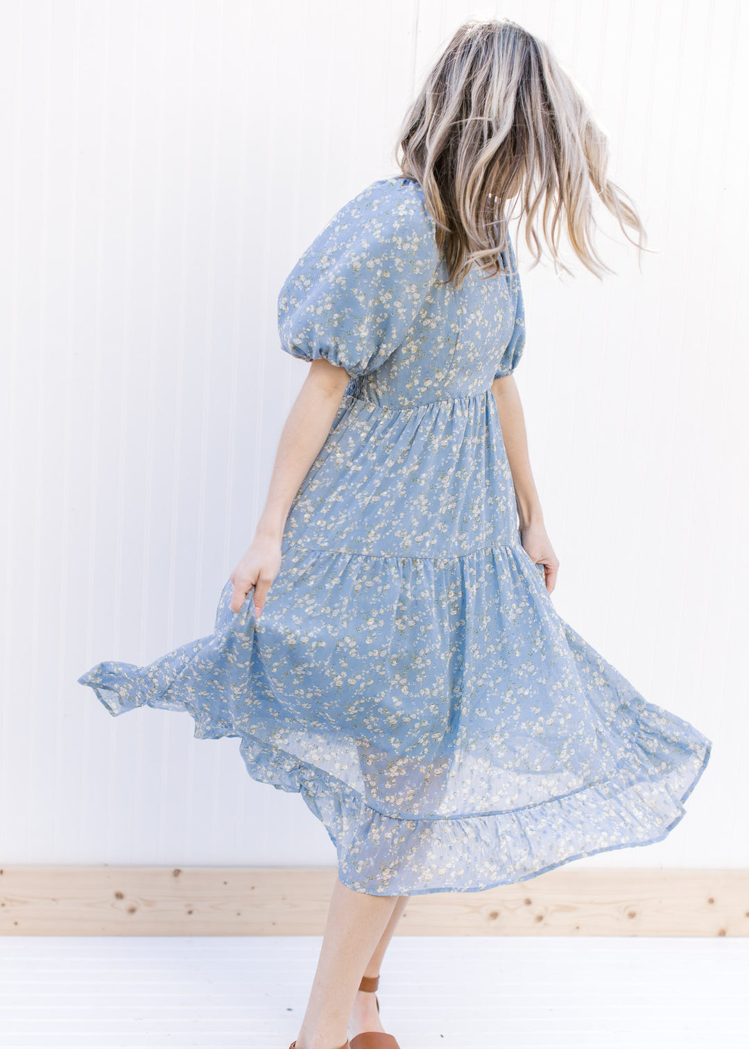 Model wearing heels with a baby blue tiered dress with white poppy flowers and square neckline.