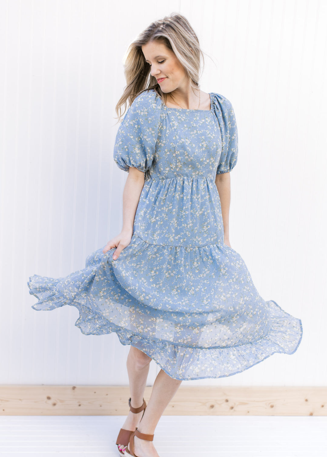 Model twirling in a baby blue tiered dress with white poppy flowers and a square neckline.