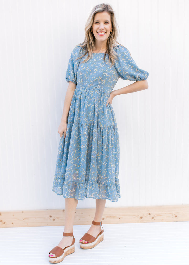 Model wearing a polyester baby blue dress with white poppy flowers and bubble short sleeves.