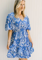 Model wearing a blue and white above the knee dress with a porcelain pattern and bubble short sleeve