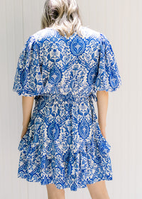 Back view of Model wearing a blue and white dress with a porcelain pattern and bubble short sleeves.