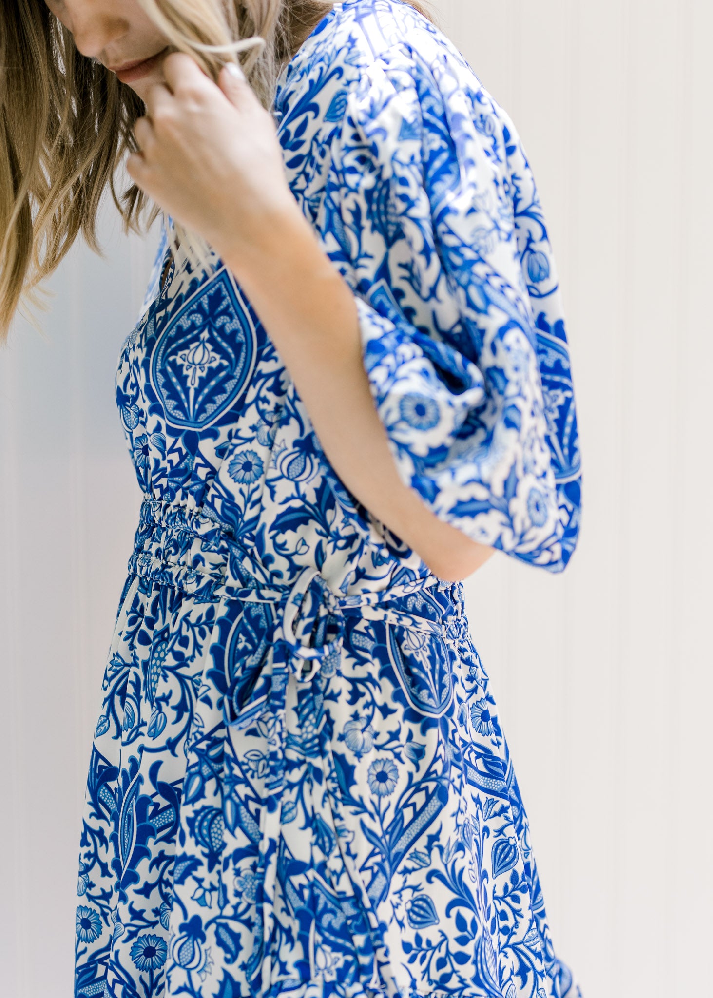 Close up of tie on side at waist on a blue and white porcelain pattern dress. 