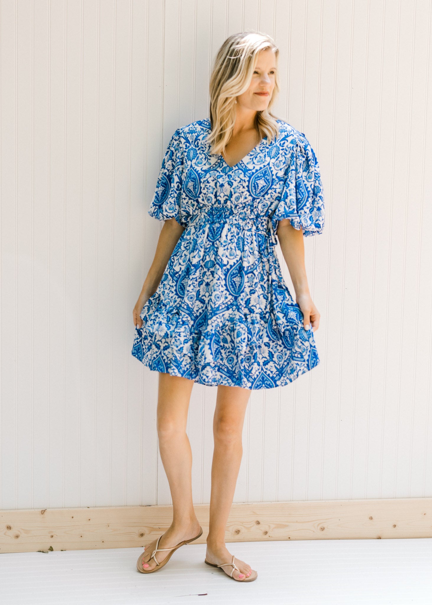 Model wearing a blue and white v-neck dress with a porcelain pattern and bubble short sleeves.