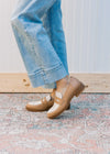 Side view of a model wearing taupe and almond loafers with a flat block heel and coin detail. 