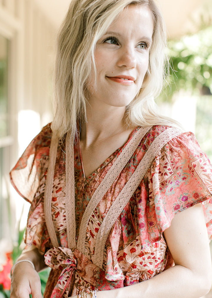 Close up of beige lace v-neck detail and flutter cap sleeves on a maroon midi with patchwork. 