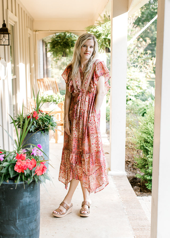 Model wearing heals and a maroon midi with patches, floral hues, v-neck and flutter short sleeves.