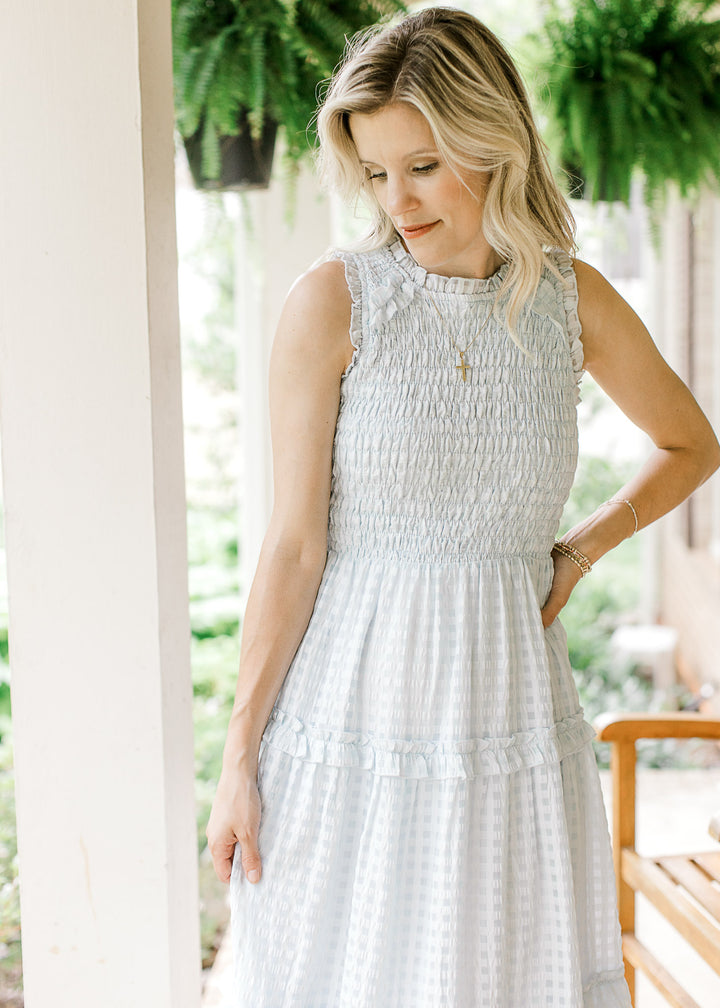 Model wearing a sleeveless powder blue midi with a smocked bodice, checks and a tiered skirt.